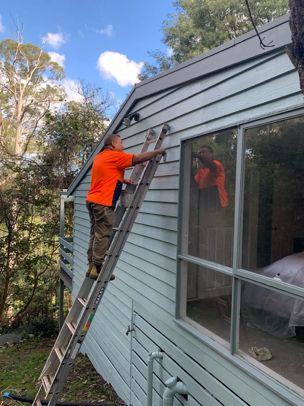Painter working on a weatherboard home exterior